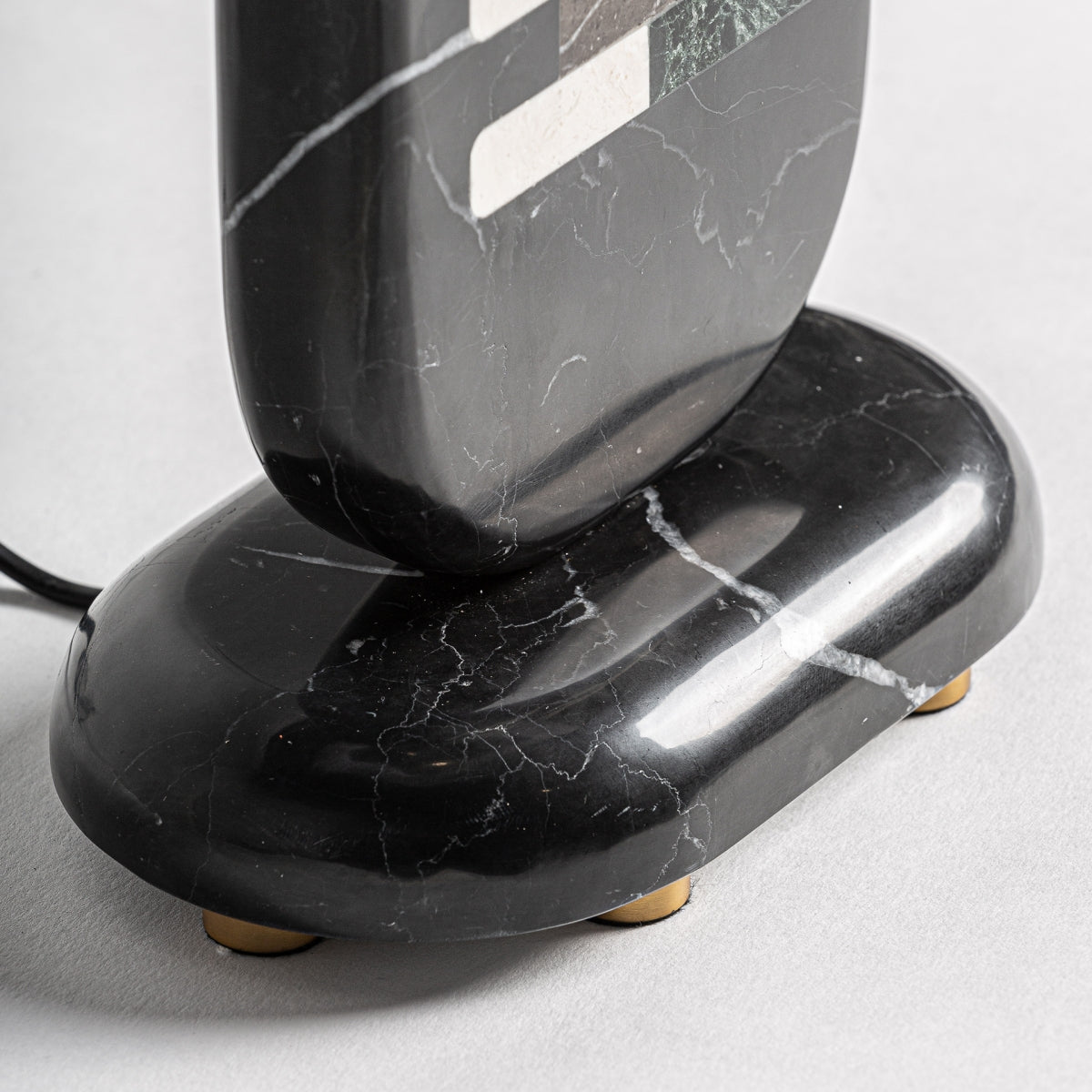 Lámpara de mesa fabricada de mármol negro y metal dorado, con pantalla de poliéster.