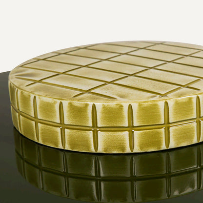 Mesa auxiliar ovalada con pie circular en metal tallado en cuadros verde amarillo.