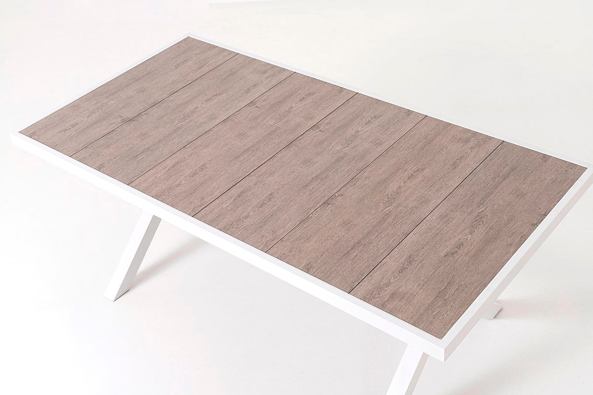 Mesa de comedor exterior, fabricada de aluminio blanco y tapa de cerámica efecto madera.
