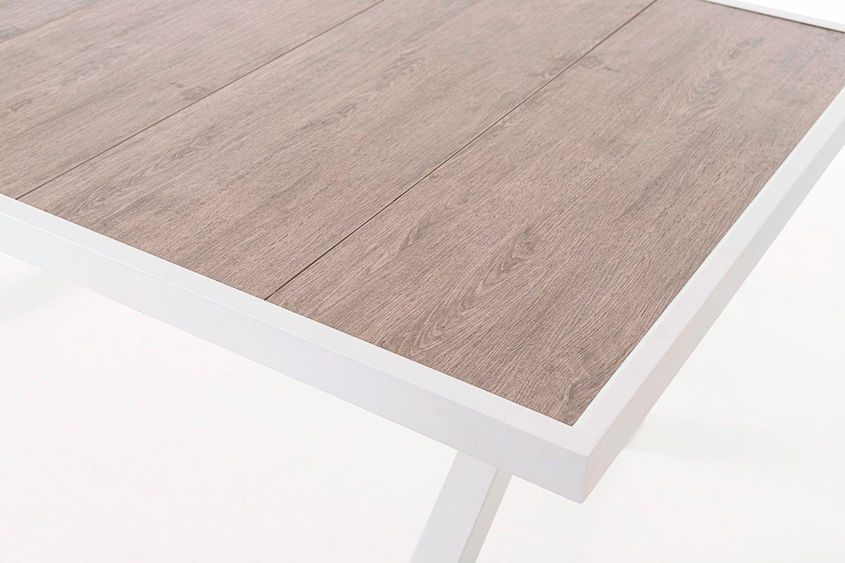 Mesa de comedor exterior, fabricada de aluminio blanco y tapa de cerámica efecto madera.