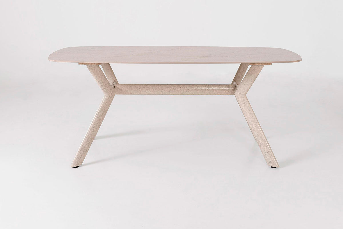 Mesa de comedor outdoor, con un diseño minimalista. Fabricada de metal con tapa de porcelánico ovalada en color beige con pequeñas vetas.